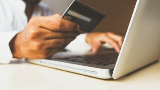 クレジットカードを手に持ちながらノートパソコンでオンラインショッピングをする男性