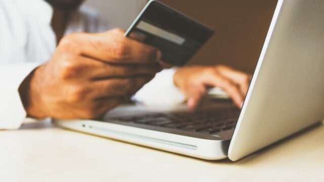 クレジットカードを手に持ちながらノートパソコンでオンラインショッピングをする男性