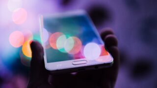 カラフルなボケ光の中でスマートフォンを持つ手。モバイル通信のイメージ