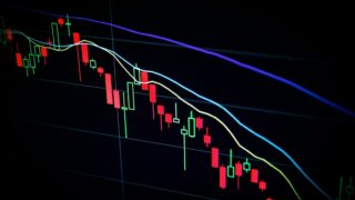 赤と緑のローソク足チャートに移動平均線が重なった株価チャート画面。右肩下がりのトレンドを示す一例のイメージ