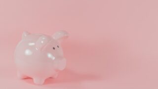 ピンク色の陶器製貯金箱。ピンクの背景の上に置かれ、コツコツ積立を続けるイメージを表す